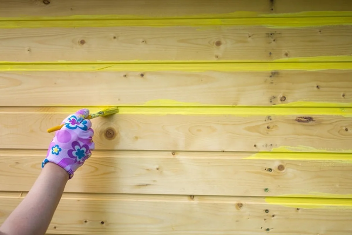 Dziewczyna maluje drewnianą ścianę żółtą farbą