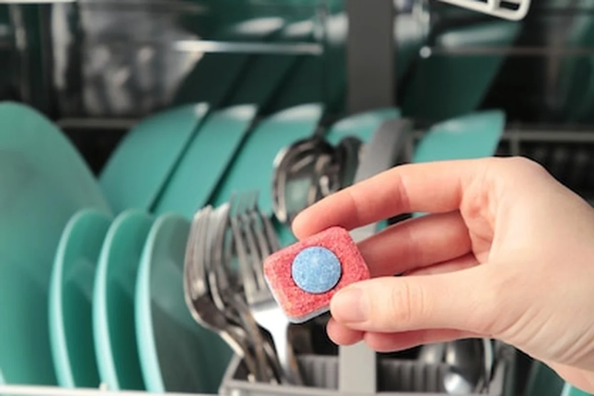 Tabletka do zmywarki w ręku obok otwartej zmywarki